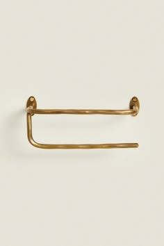 a gold colored metal hook on a white wall with the handle extended to it's left side