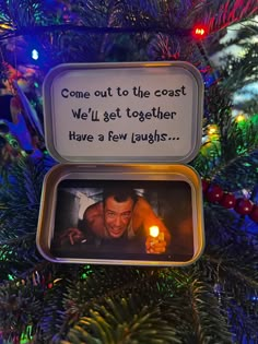 an ornament hanging on a christmas tree with a candle in the foreground that reads, come out to the coast we'll get together have a few laughs