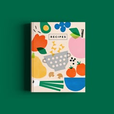 a cookbook with an illustrated image of fruits and vegetables on it, sitting against a green background