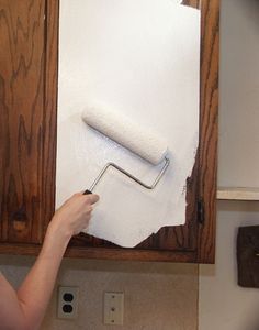 a woman is painting the wall in her kitchen with white paint and a roll of paper