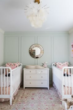 two white cribs in a green room with pink and gold decor on the walls