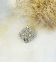 a silver pendant with an intricate design on it's end and a fur ball in the background