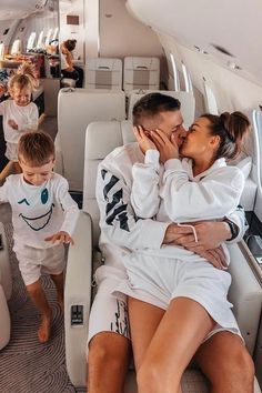 a man and woman kissing while sitting on an airplane with two children in the aisle