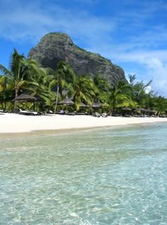 the beach is surrounded by palm trees and umbrellas, with a mountain in the background