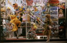 a woman standing in front of a store window with stuffed animals and toys on display