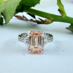 a fancy pink diamond ring sitting on top of a leafy green plant next to it