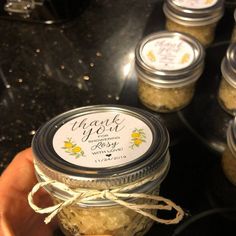 a hand holding a jar filled with honey on top of a counter next to other jars