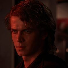 a young man with red hair and blue eyes stares at the camera in a dark room