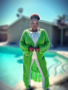 a woman standing in front of a pool wearing a green cardigan and white pants