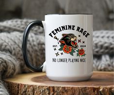 a black and white coffee mug sitting on top of a wooden table next to a gray sweater