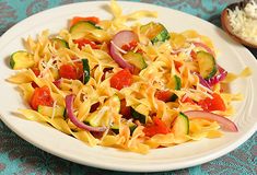 a white plate topped with pasta and veggies on top of a blue table cloth