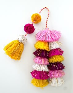 multicolored tassels hanging from string on white surface with red and yellow pom - poms