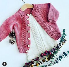 a pink sweater and white sweater sitting on top of a wooden hanger next to flowers