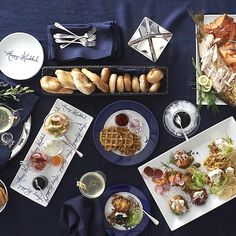 an assortment of food is laid out on a blue tablecloth with silverware and napkins