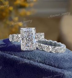 an engagement ring and wedding band set on top of a blue velvet box with flowers in the background