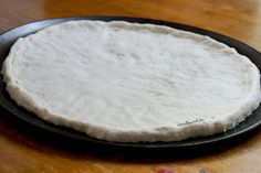 a black plate on a wooden table with a pizza crust in the middle, ready to be baked