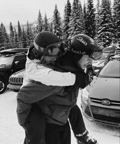 two people are hugging each other in the snow with helmets on and one person is wearing skis