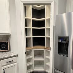 an empty pantry in the corner of a kitchen with stainless steel refrigerator and white cabinets