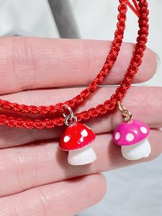 a hand holding a red string with two small mushroom charms on it's end