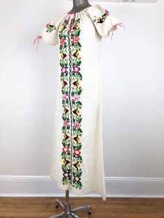 "1970s Mexican white cotton peasant dress has colorful floral embroidery down the front and around the sleeves, and a drawstring neckline and sleeve openings with pink braided yarn. Condition Overall very good, has some dye bleed on the front next to the purple flowers, a stain at the back right shoulder, and light grey discoloration at the hem from wear. All of the drawstring ends have fray. Measurements Bust 38\" Waist 35\" Hip 39\" Sleeve length 10\" Length 54\"" Folk Style Embroidered Dress With Embroidered Sleeves For Spring, Spring Folk Embroidered Dress With Embroidered Sleeves, Spring Peasant Long Dress, Traditional Spring Daywear Dress, Long Peasant Spring Dress, Spring Long Peasant Dress, Spring Peasant Embroidered Dress With Multicolor Embroidery, Bohemian Cotton Embroidered Dress For Daywear, Spring Folk Style Cotton Embroidered Dress