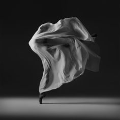 a black and white photo of a woman's dress blowing in the wind on a dark background