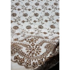 a white table cloth with gold beading and flowers on the top, in front of a