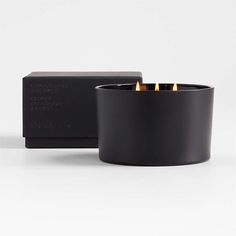 a black candle holder with three candles in it and a box behind it on a white surface