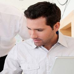 a man is looking at his laptop screen while another man looks down on the computer