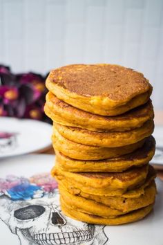 a stack of pancakes sitting on top of a white plate next to a purple flower