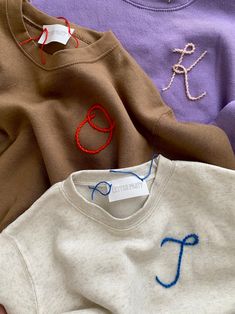 three sweaters with different colored thread on them, one is white and the other is brown