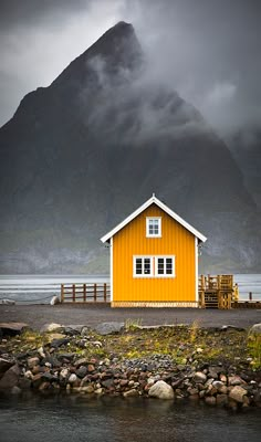 a yellow house sitting on top of a rocky beach next to a body of water