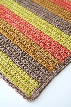 a multicolored crocheted dishcloth on a white table top with the colors of brown, yellow, red, and orange