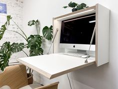 an apple computer sitting on top of a white desk next to a potted plant