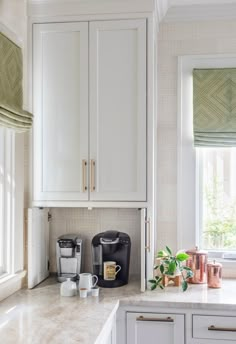 a kitchen with white cabinets and marble counter tops, along with a coffee maker in the corner