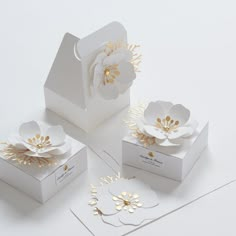 three white boxes with gold flowers on the top and one has a flower in it