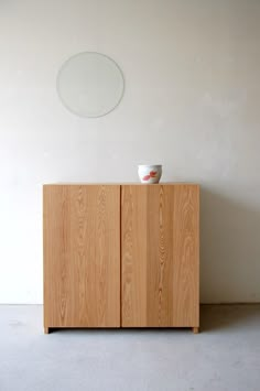 a wooden cabinet with a cup on top and a white wall in the back ground