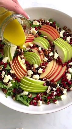 someone is pouring dressing into a salad with apples and cranberries in a white bowl