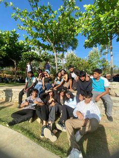 a group of people sitting and standing around each other on the grass with trees in the background