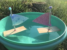 two paper boats are sitting in a blue bowl filled with water and some sticks sticking out of it