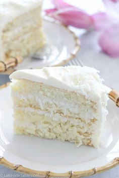 a slice of coconut cake with white frosting on a plate next to a fork