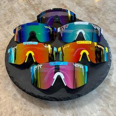 three pairs of colorful sunglasses sitting on top of a black stone plate with two different colored lenses