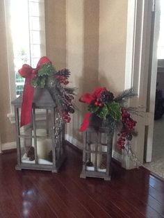 two metal lanterns decorated with red bows and pine cones are sitting on a wood floor