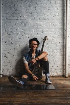 a man sitting on the floor with his bass in front of him and wearing a hat