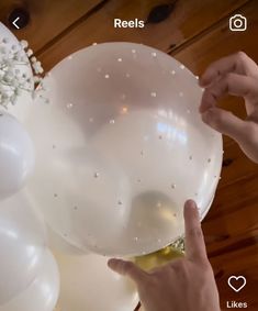 someone is decorating balloons with white flowers and pearls on the bottom, while another person points at them