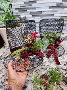 two wire baskets with pine cones and evergreens in them are sitting on a table