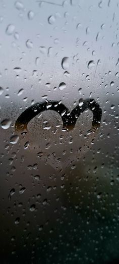 the word love is written in black on a wet window with drops of water around it