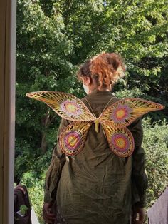 a woman in green jacket with butterfly wings on her back, looking out the window