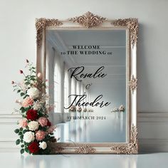 a wedding welcome card with flowers in front of a mirror