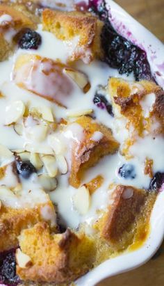 blueberry bread pudding in a white bowl on a wooden table with cream drizzled over it