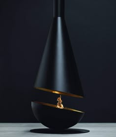 a black vase with a fire in it on top of a white table next to a dark wall